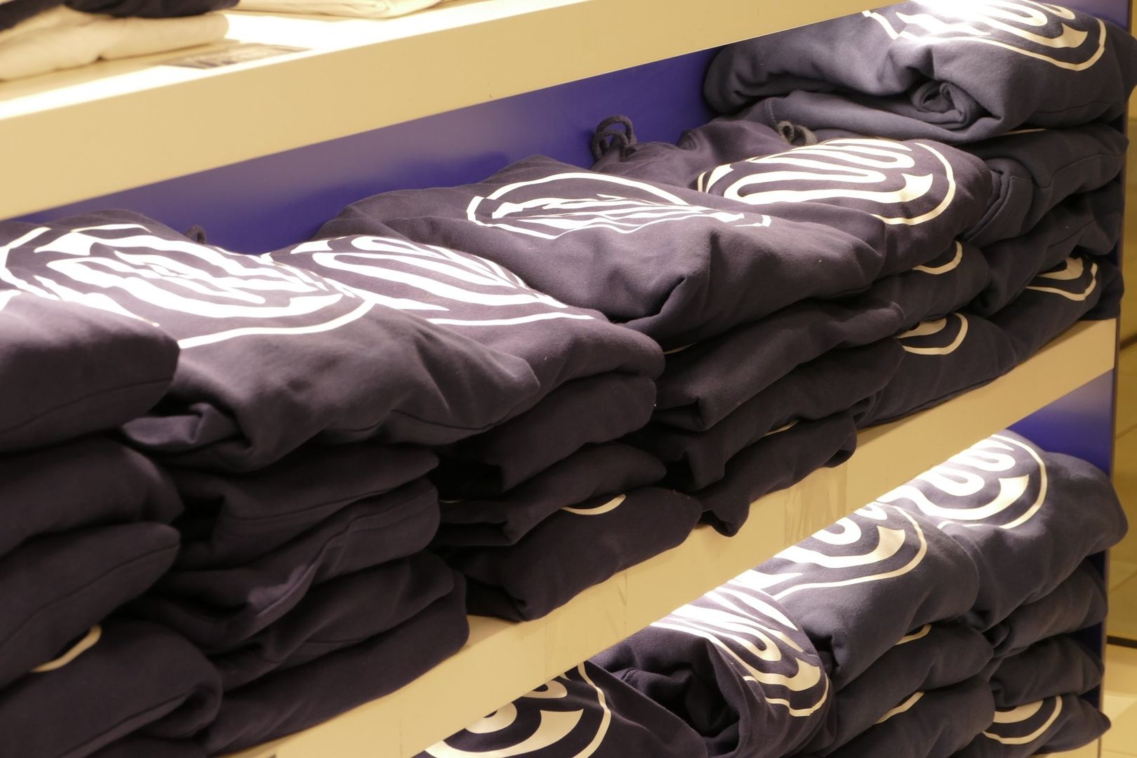 Gefaltete schwarze Hoodies mit einem weißen Aufdruck liegen ordentlich gestapelt in einem Regal.